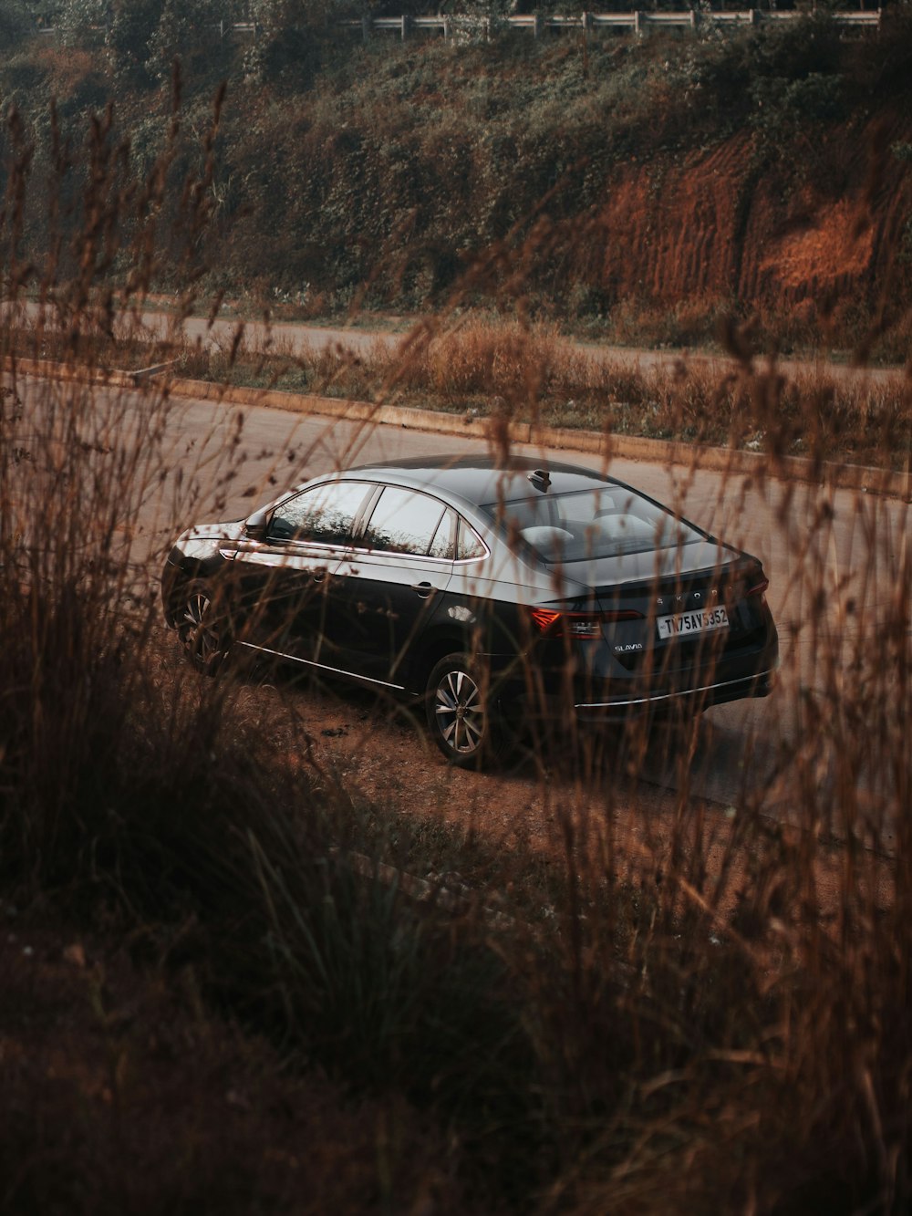 a black car driving down a road next to tall grass