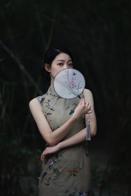 Elegant Chinese woman holding a traditional fan in cheongsam dress, representing the qipao fashion legacy