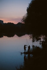 Members teaching children how to fish by a calm lake at sunset.