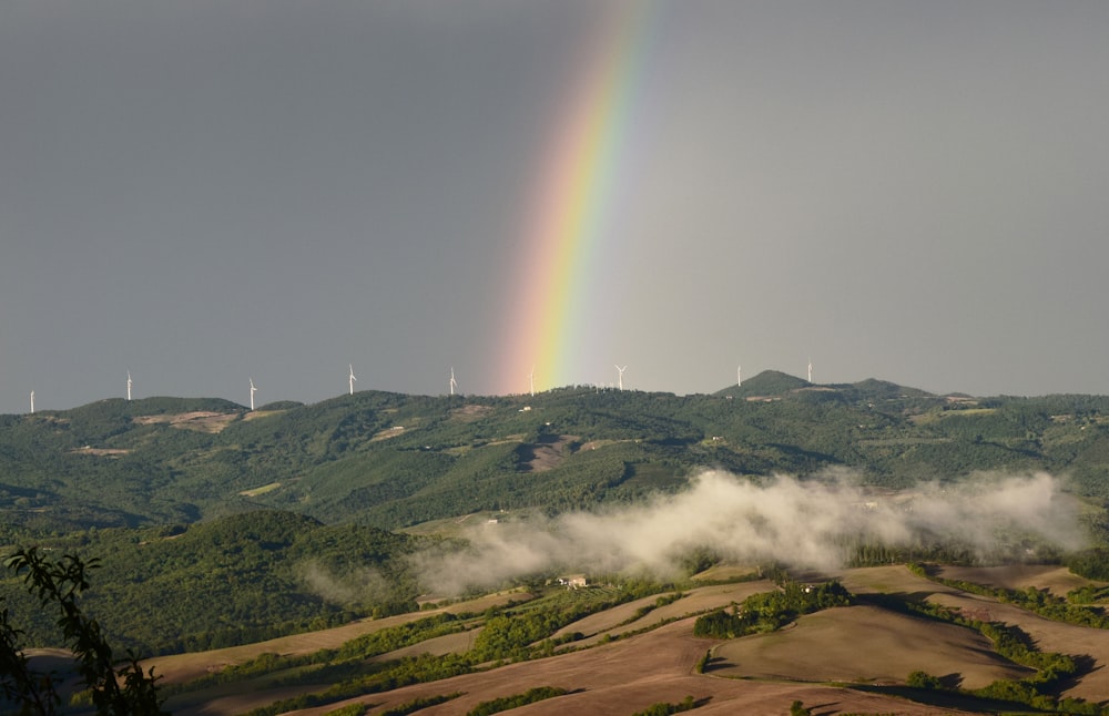 a rainbow shines in the sky over a hilly area