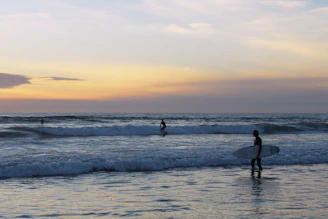 Surfers catching waves at a pristine beach near Selong Belanak at sunset.