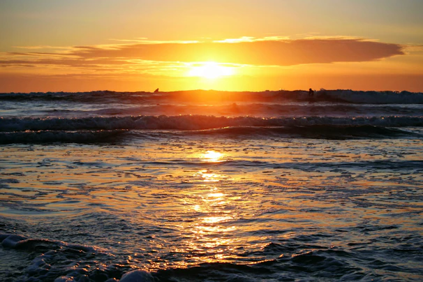 A vibrant sunset over a California beach with surfers catching waves.