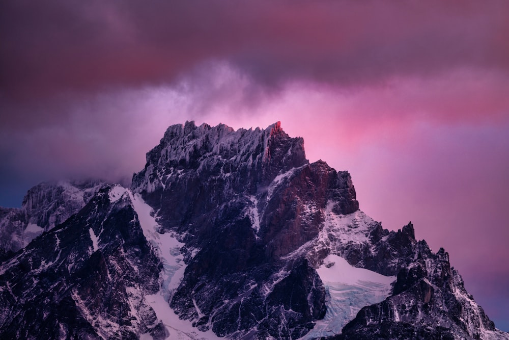 a very tall mountain covered in snow under a cloudy sky