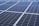 A close-up view of a large array of solar panels, with a uniform pattern of dark blue photovoltaic cells arranged in a grid. The panels are lined with silver frames, reflecting sunlight and indicating a clear day.