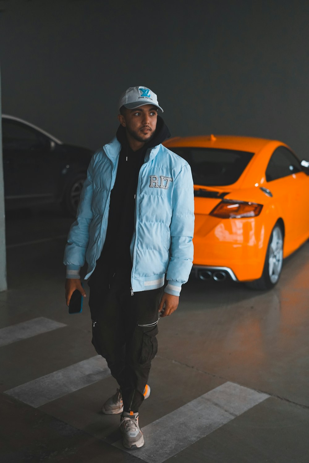 a man standing in a parking garage next to an orange sports car