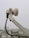 A close-up of a white satellite dish arm and its attached components, including a cable that stretches downward. The background shows an urban landscape with buildings that appear slightly blurred due to depth of field.