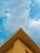 A triangular rooftop against a backdrop of a partly cloudy sky. The roof is painted in a soft yellow color, creating a contrast with the blue sky and white clouds.