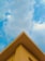 A triangular rooftop against a backdrop of a partly cloudy sky. The roof is painted in a soft yellow color, creating a contrast with the blue sky and white clouds.