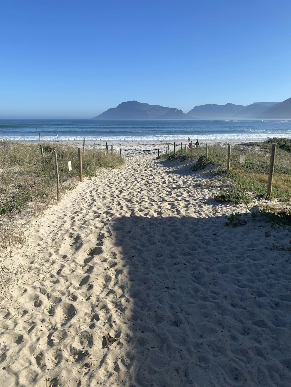 a sandy path leading to the beach with mountains in the background