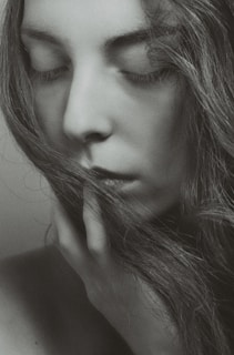 A black and white portrait of a person with closed eyes, serene expression, and long hair partially covering the face. The hand gently touches the chin, evoking a sense of calm and introspection.