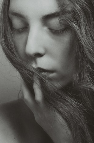 A black and white portrait of a person with closed eyes, serene expression, and long hair partially covering the face. The hand gently touches the chin, evoking a sense of calm and introspection.