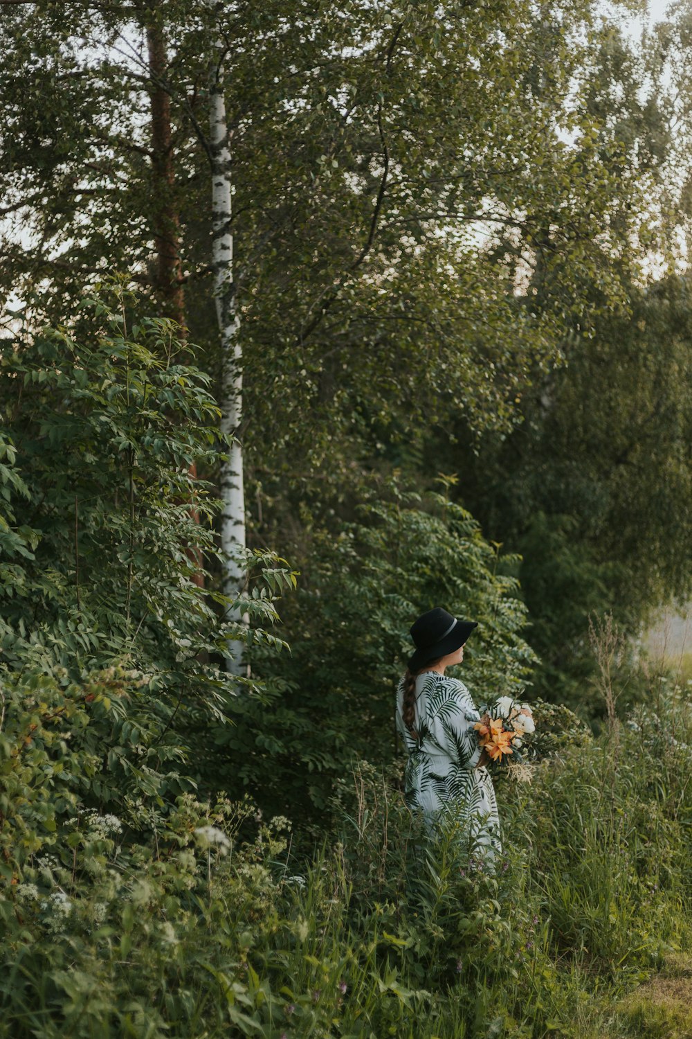 a woman in a dress and hat walking through a forest
