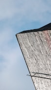 An angled view of a building's rooftop with weathered, vertically-aligned bricks against a blue sky. The rooftop features some dark edges and appears slightly overcast.