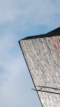 An angled view of a building's rooftop with weathered, vertically-aligned bricks against a blue sky. The rooftop features some dark edges and appears slightly overcast.