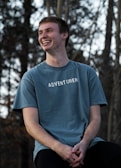 Smiling man outdoors wearing a Korpa t-shirt, enjoying fresh air.
