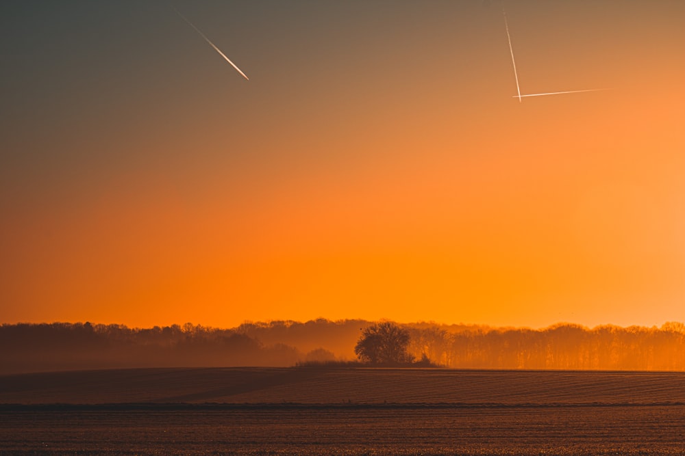 the sun is setting over a field with trees