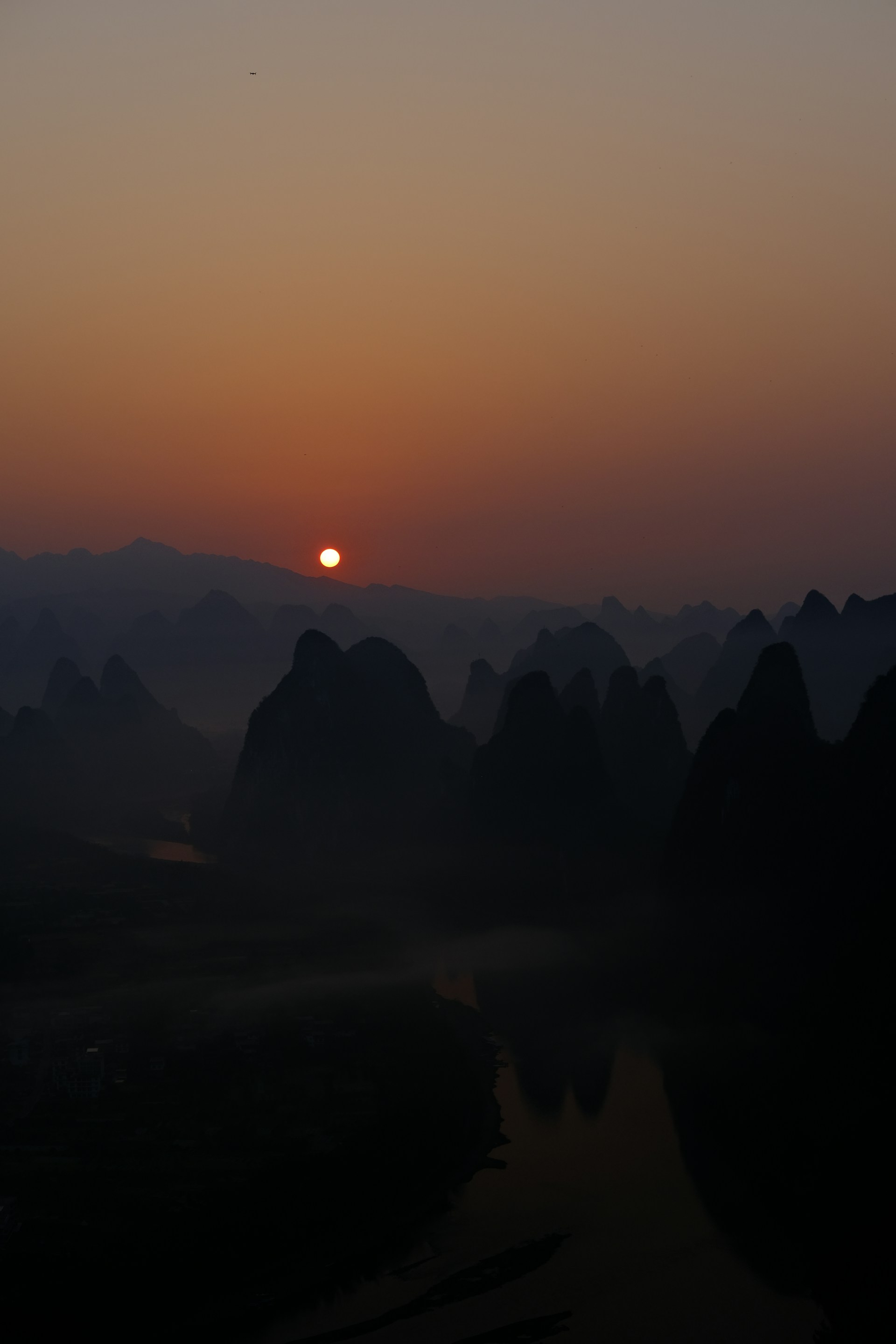 A serene view of the Li River with karst mountains reflecting in the calm water during sunrise.