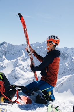 A friendly ski instructor helping a client prepare their gear on a snowy mountain slope.