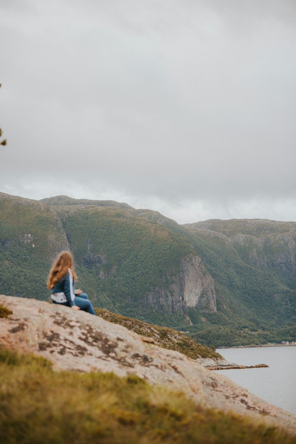 a woman sitting on top of a rock next to a body of water