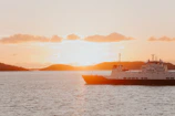 Golden sunset reflecting off calm waters as a ferry sails toward a lush island.