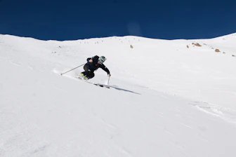 A skier wearing advanced protective gear, including a sensor-equipped helmet, gliding down a snowy slope.
