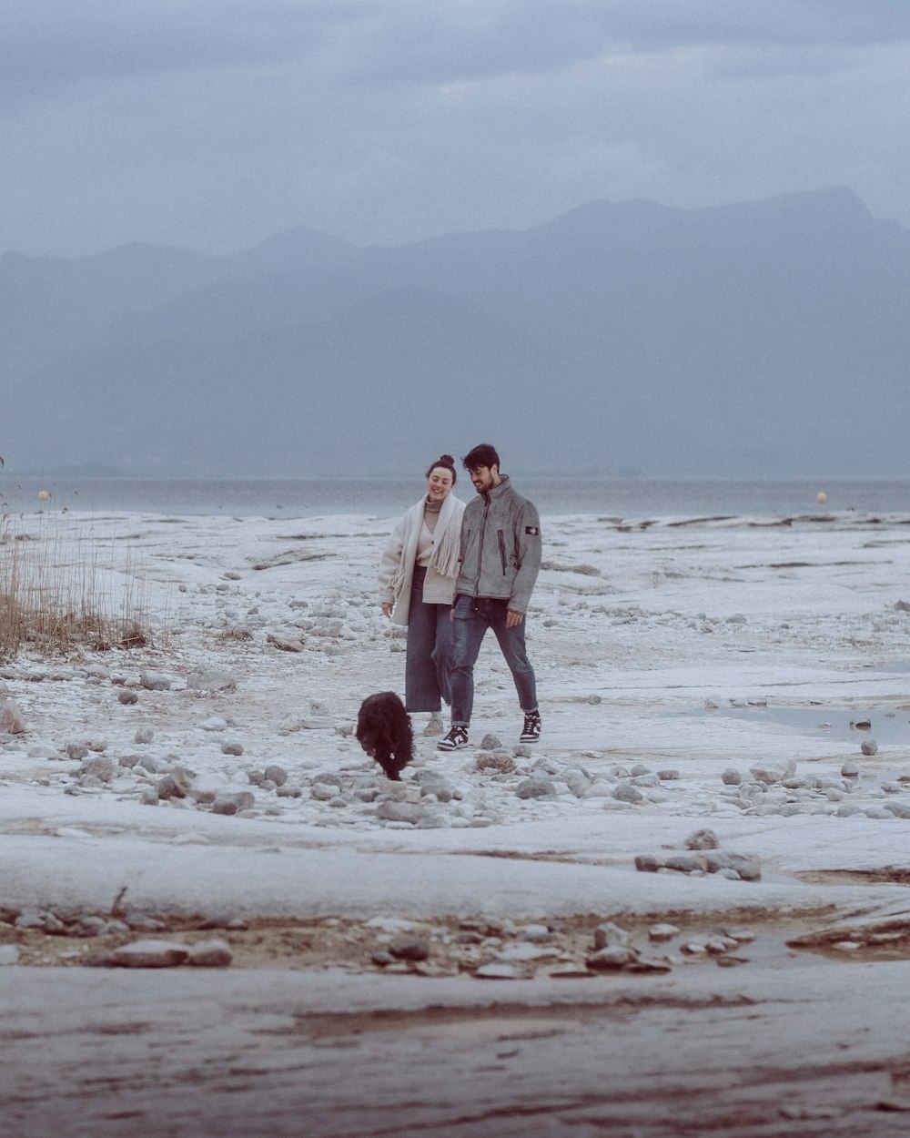 a man and a woman standing in the snow with a dog