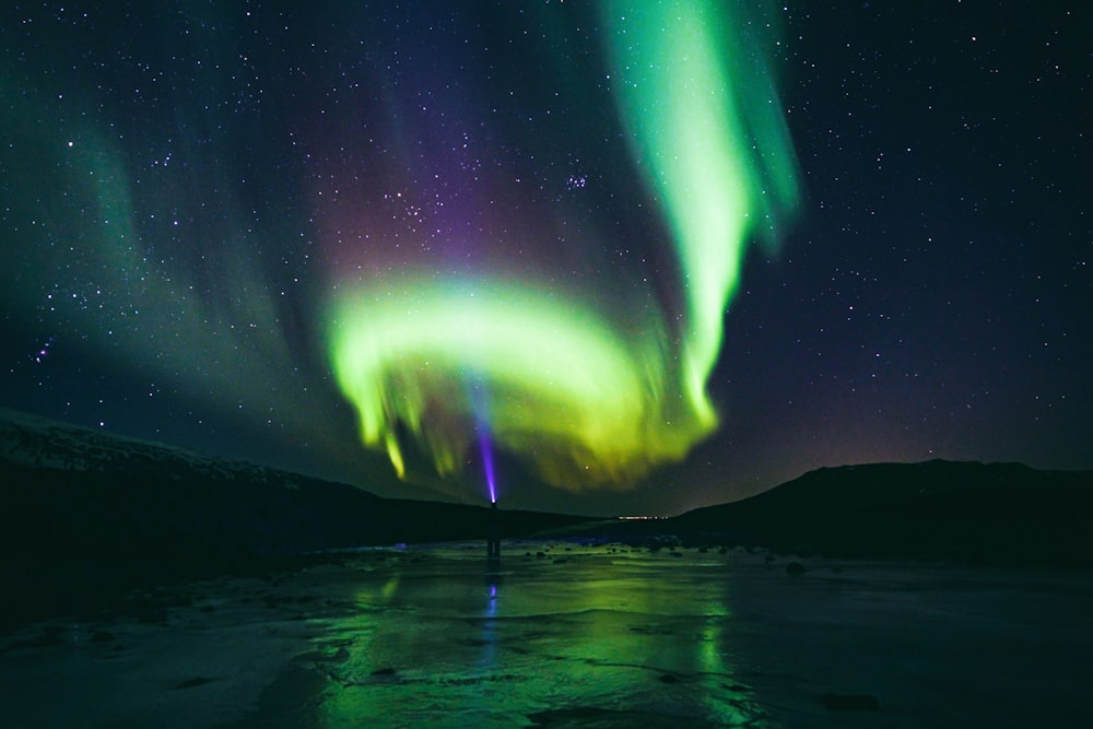 uma pessoa de pé em um lago congelado sob uma aurora verde e roxa furada