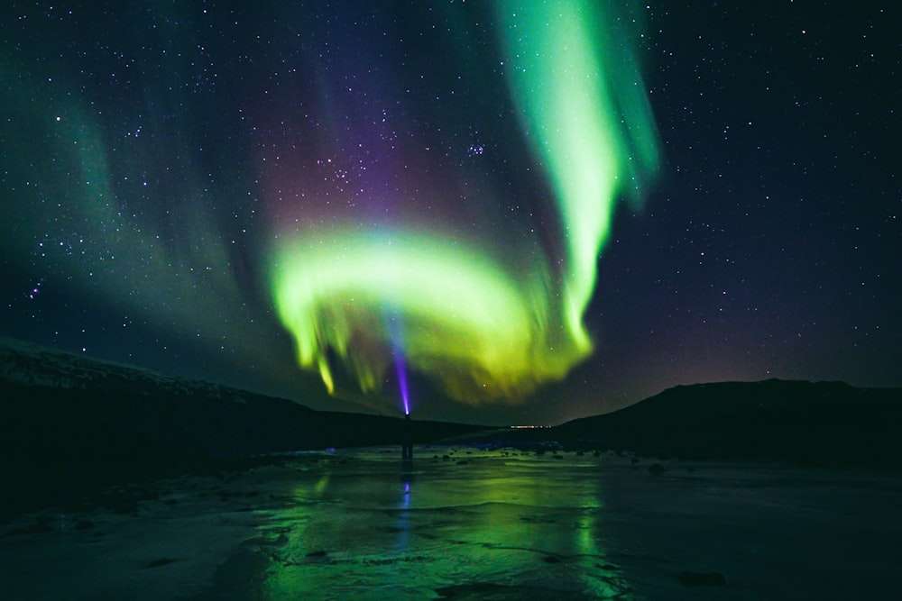 a person standing on a frozen lake under a green and purple aurora bore