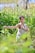 A person is practicing a martial art form in a lush green natural setting. Surrounded by tall grass and foliage, they hold a poised stance with focused concentration. Sunlight filters through the leaves, creating a serene and tranquil atmosphere.
