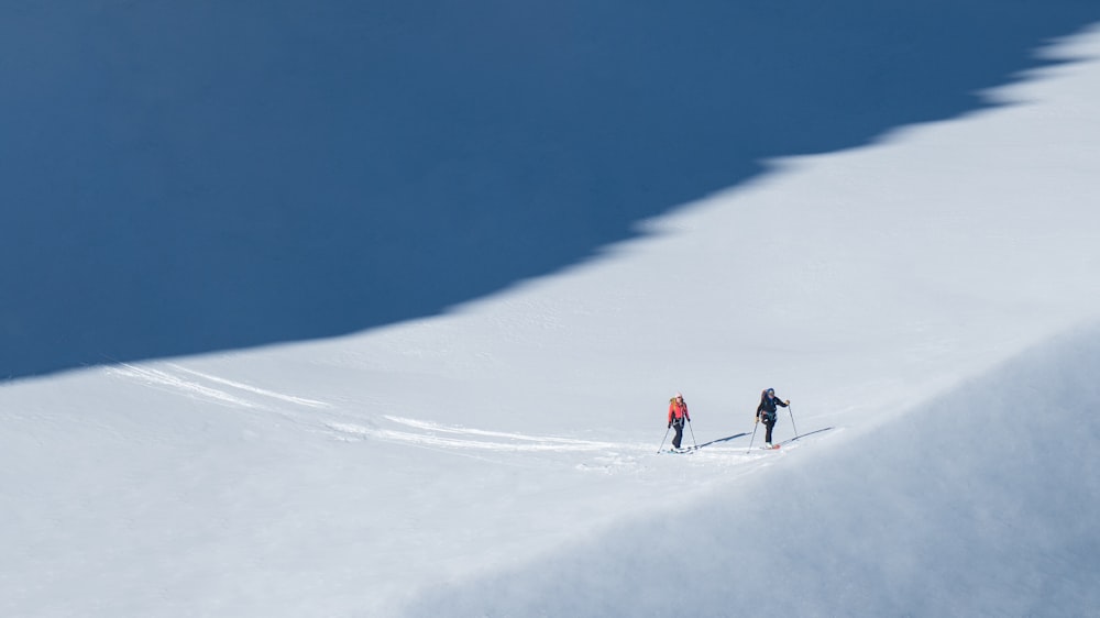 a couple of people riding skis down a snow covered slope