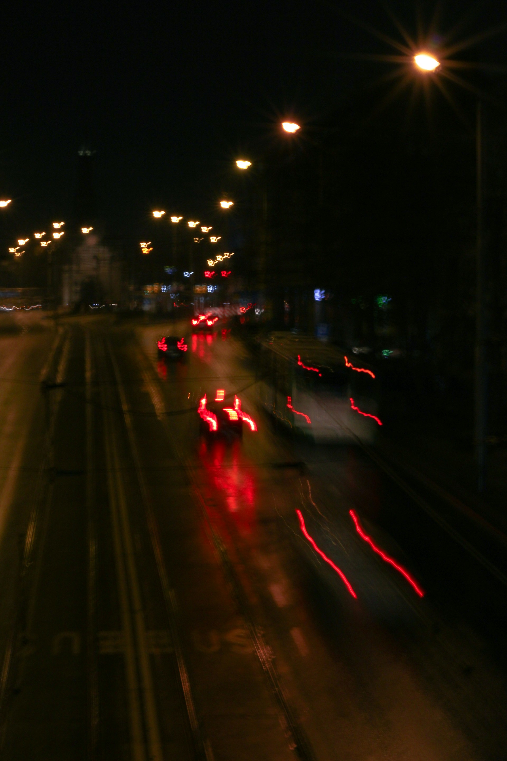 A moody black-and-white photograph capturing an urban night scene with subtle red light accents.