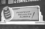 A vintage advertisement on a brick wall promoting Magic Baking Powder. The design includes a large illustration of a tin of the product, with bold text stating 'Perfect Results Always!' The advertisement uses a classic font style, with a monochromatic color scheme.