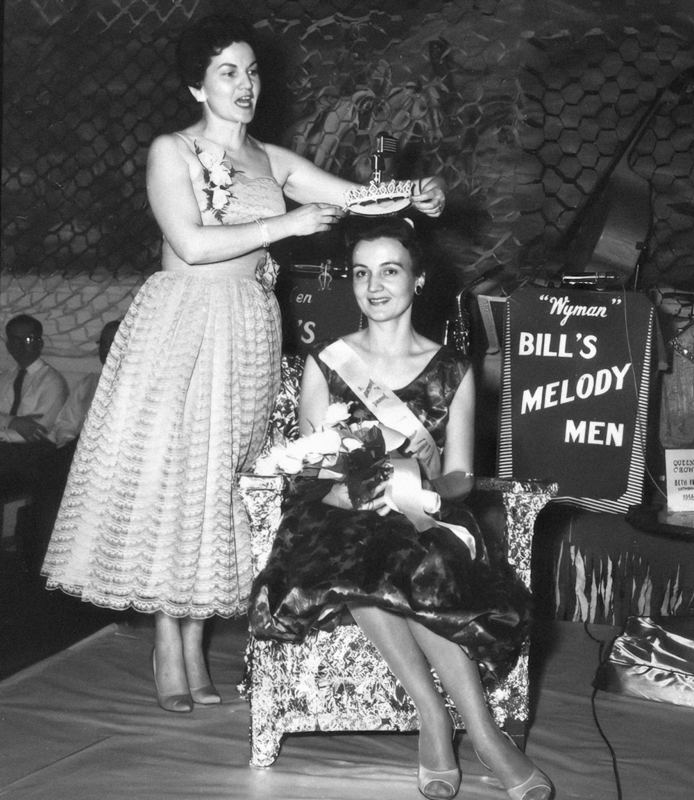 a woman sitting in a chair while another woman holds a cake