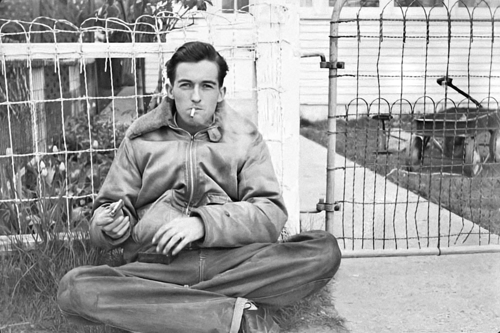 a man sitting on the ground in front of a fence