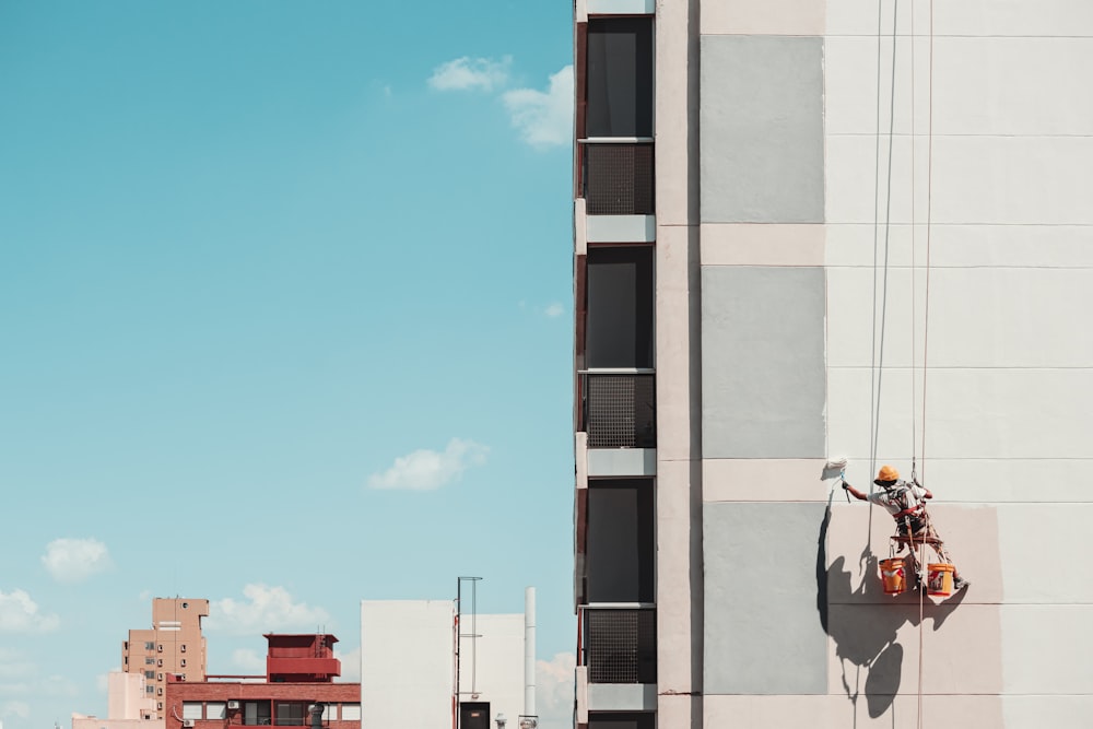 Un hombre en una escalera pintando el costado de un edificio