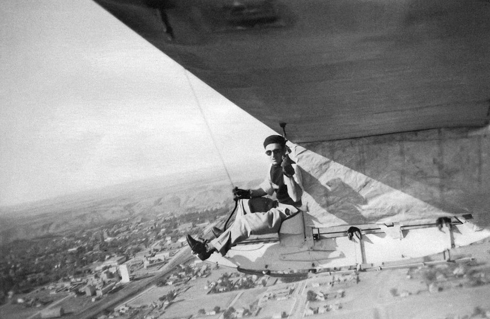 a black and white photo of a man sitting on the wing of a plane