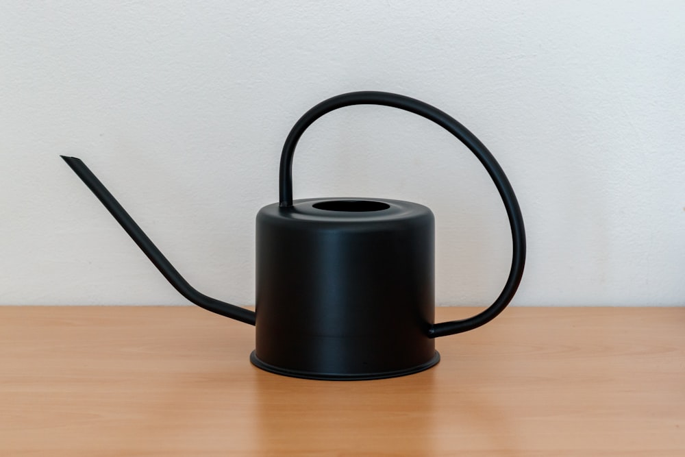 a black watering can sitting on top of a wooden table