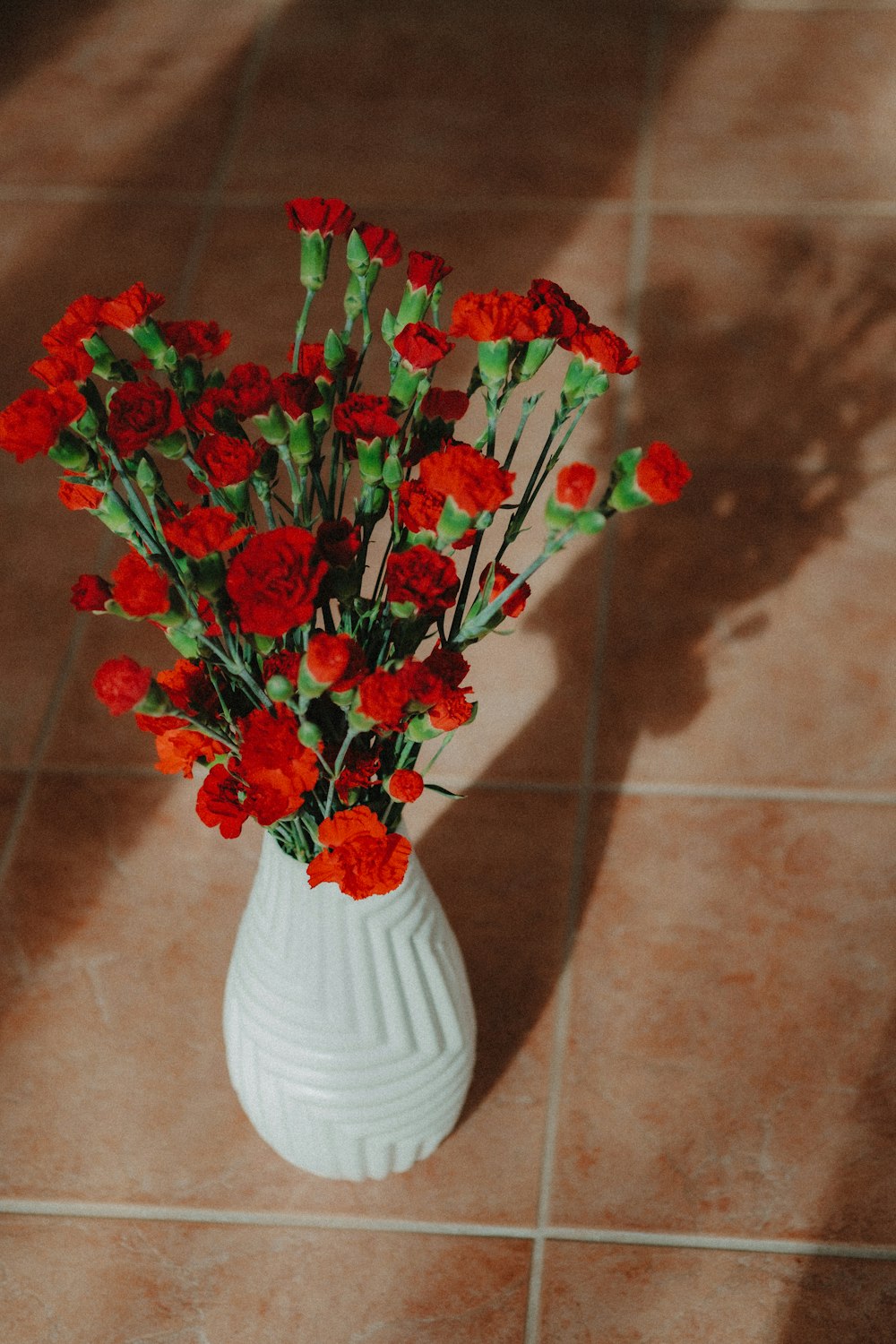 a white vase filled with red flowers on a tile floor