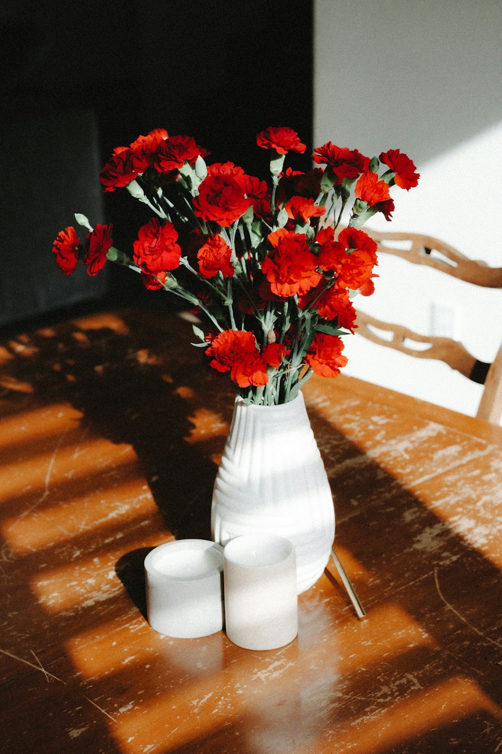 a white vase filled with red flowers on top of a wooden table