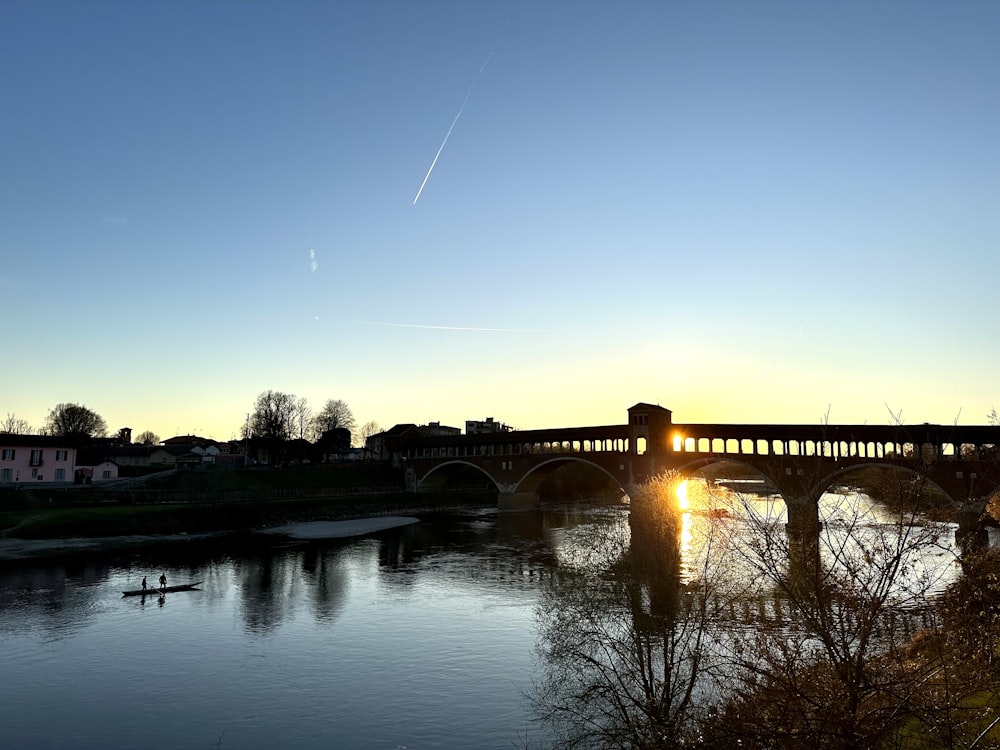 the sun is setting over a bridge over a river