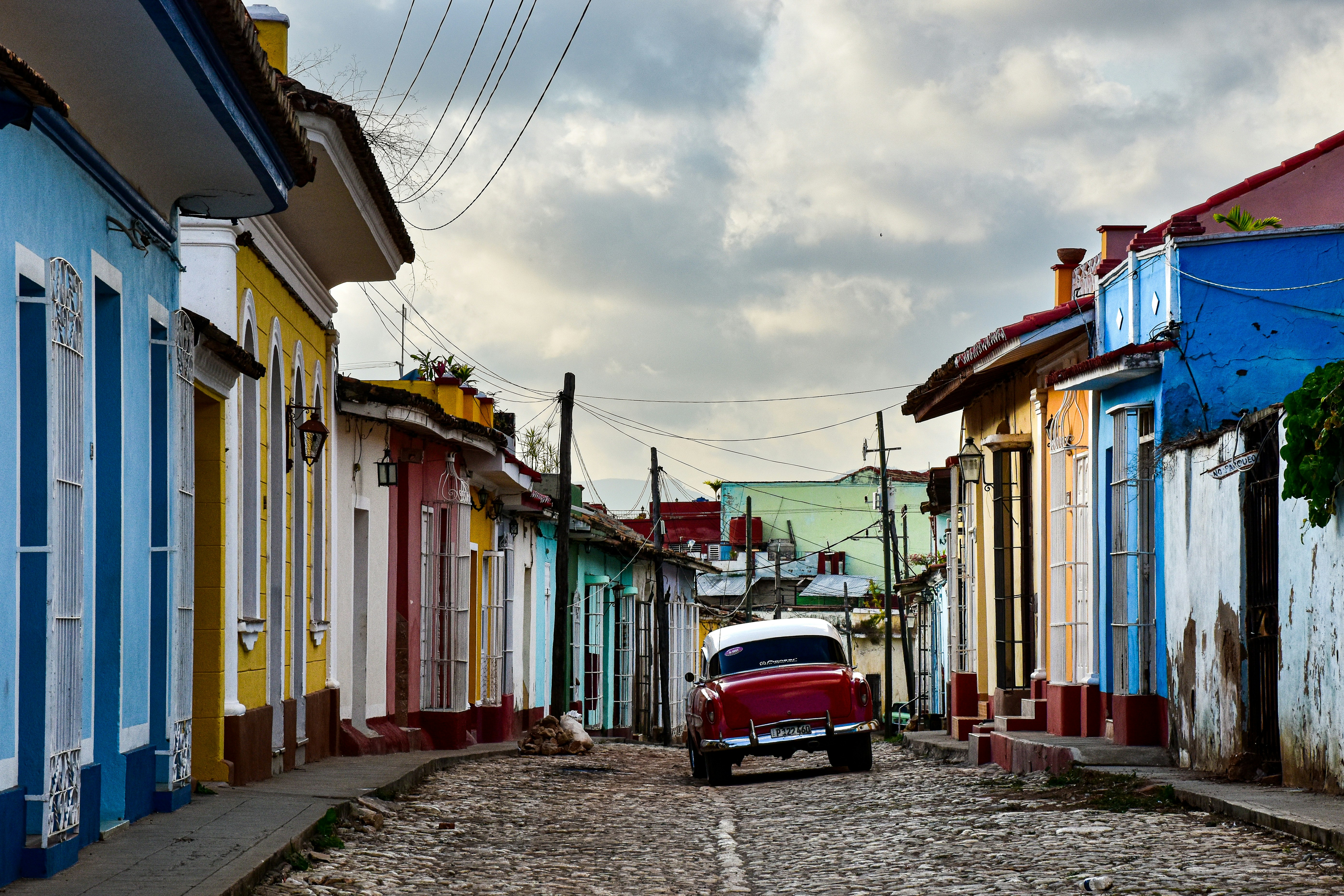 a red car is parked on a cobblestone street, Trinidad, Cuba.