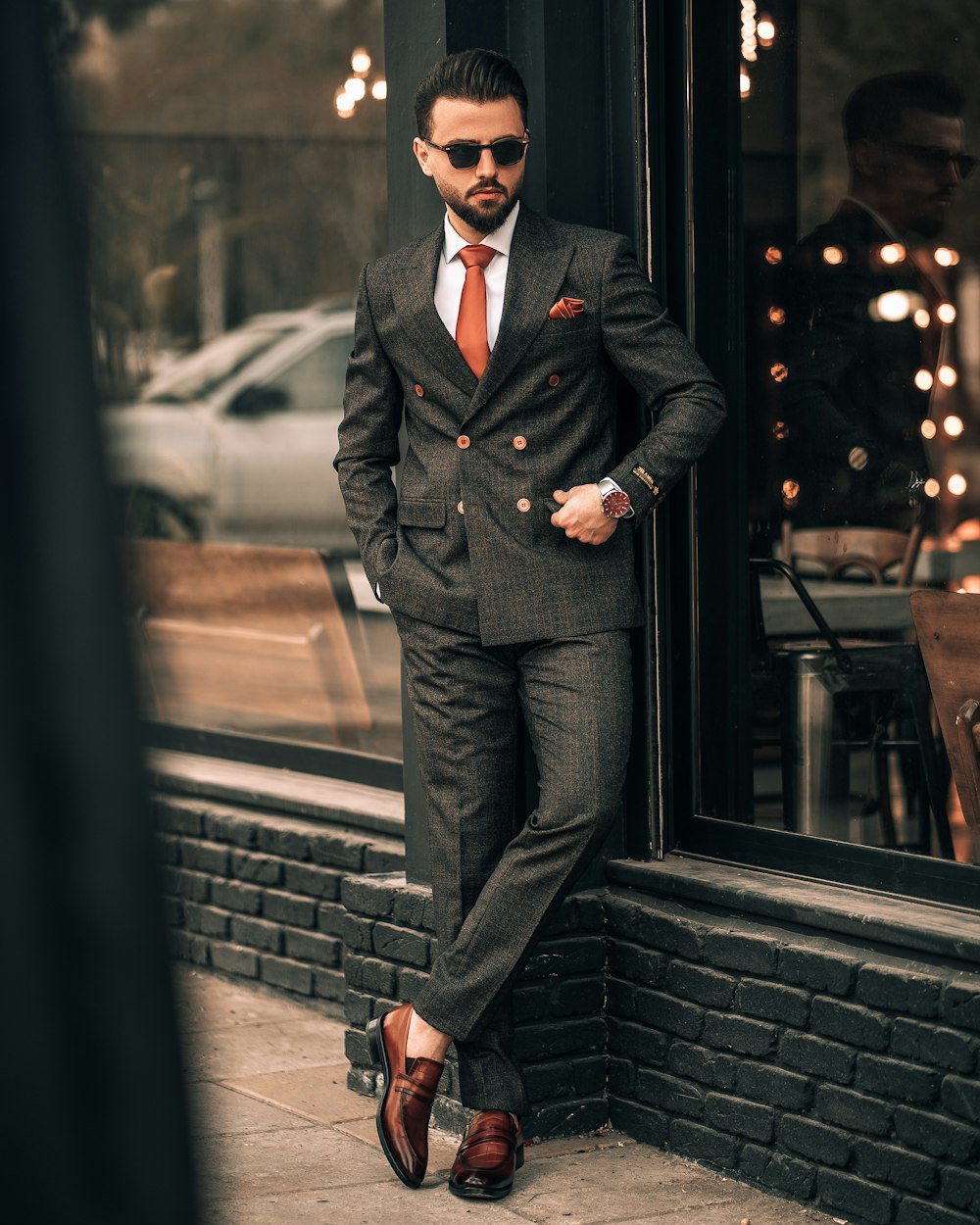 a man in a suit leaning against a brick wall