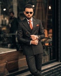 a man in a suit and sunglasses standing in front of a window