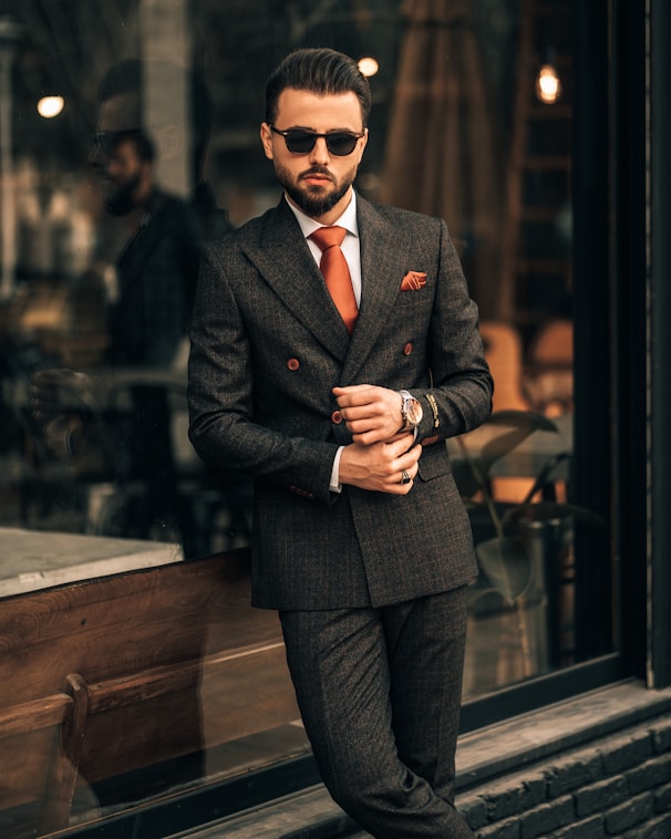 a man in a suit and sunglasses standing in front of a window