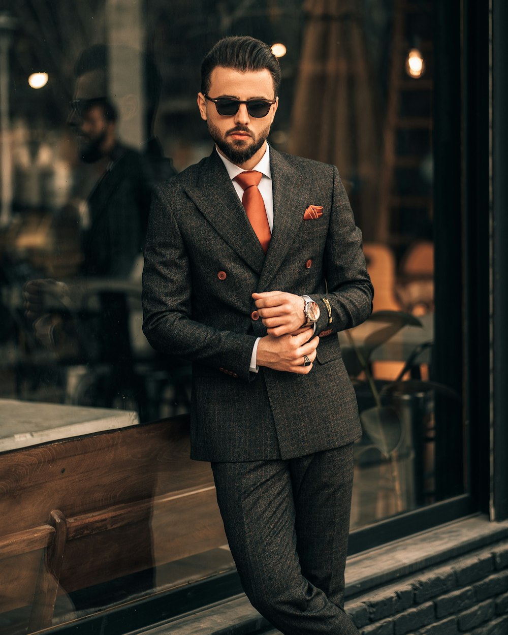 a man in a suit and sunglasses standing in front of a window