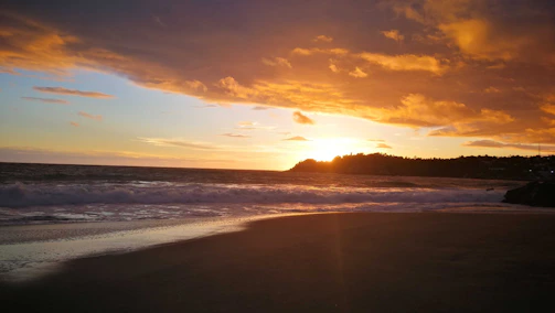 A vibrant beach scene at sunset with golden light reflecting on blue waves.