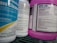 Several bottles of cleaning products are arranged close together on a shelf. Labels on the bottles provide information about the contents, warnings, and usage instructions. The prominent colors are blue and purple, with detailed text visible on the labels.