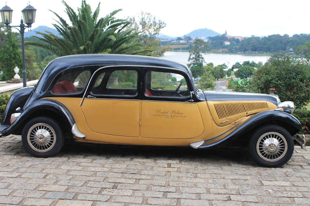 an old yellow car parked on a brick road