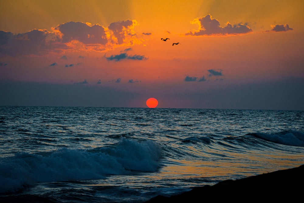 a sunset over the ocean with birds flying in the sky