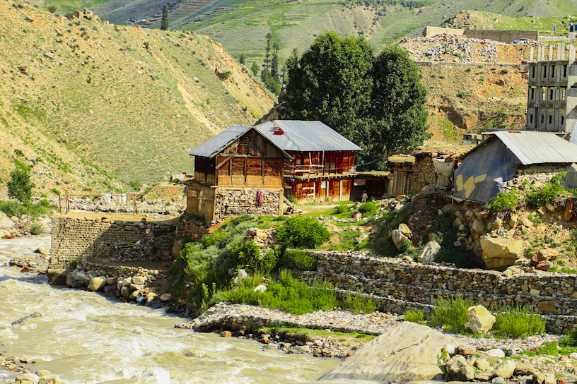 A cozy wooden homestay nestled beside a gently flowing river in Himachal Pradesh.